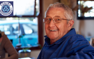 A senior man is sitting in his own home, happy, as a result of successful long-distance caregiving.