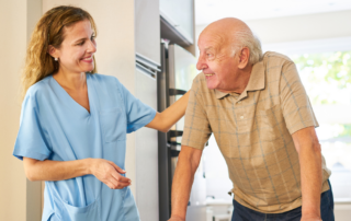 Caregiver smiling at senior man using a walker while providing senior home care services.