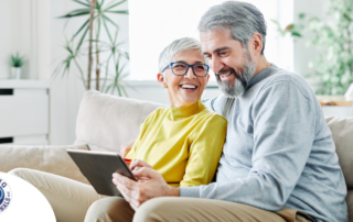 A senior couple smiles while looking at a laptop, showing how online resources can help family caregivers.