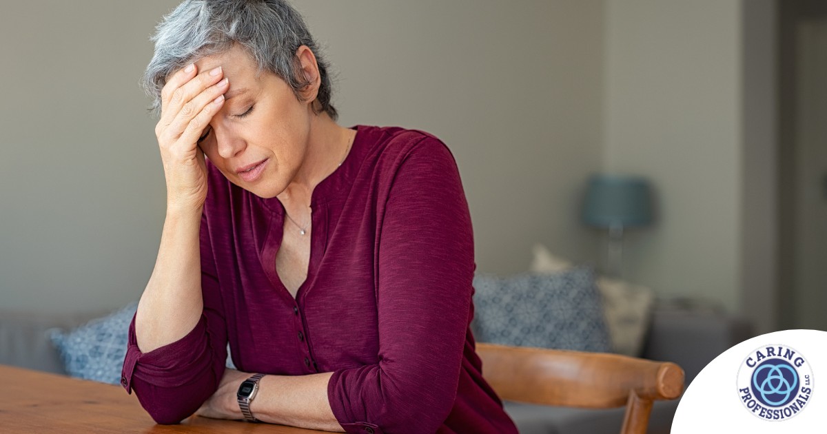 A woman holds her head in her hand, representing the stress that new family caregivers go through.